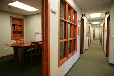 interior picture of Saks Wellness Center in Gaylord, Michigan - this picture is shot looking down the center hallway, and into one of the building's conference/consultation rooms - rich wood trim accents the calming shades of green in the walls and carpet