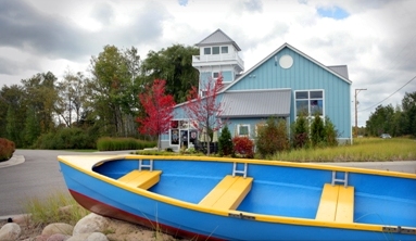 picture of Windjammer Marina in Alanson, Michigan - the light blue siding and white trim of the marina building provide a perfect backdrop for the bright blue rowboat with bright yellow seats and trim that is pulled up on the beach in the foreground of the picture