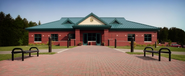 exterior picture of Alpena Combat Readiness Training Center's Headquarters Building - red brick masonry walls with green metal roof and trim, brick paver entrance walkway with bench seating