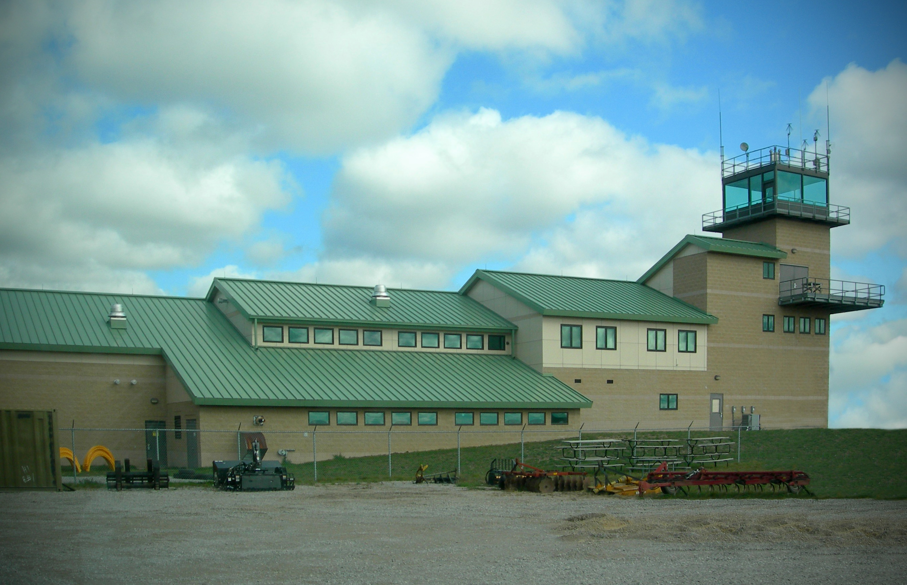 Range 40 Flank Tower Complex at Camp Grayling Annual Training Site - concrete masonry unit walls in light and dark shades of tan with green metal roof and trim, and attached control tower with observation deck