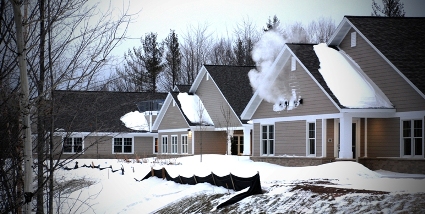 picture of Mill Creek Assisted Living Facility in Marquette MI - exterior winter picture showing the facility's rear elevation near the back tree line - snow covered ground and roofs, and clouds of steam rise from building vents