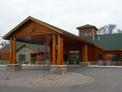 exterior picture of timber-framed porte-cochere and main entrance for Freighter View Assisted Living Facility in Sault Ste. Marie, Michigan - natural log siding and fieldstone wall construction with green shingled roof