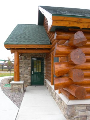 exterior photo of Freigher View Assisted Living Facility in Sault Ste. Marie, Michigan - close-up of corner timber and log framing construction, mixed carved stone siding, green shingled roof - International Bridge and Soo Locks are visible in the background