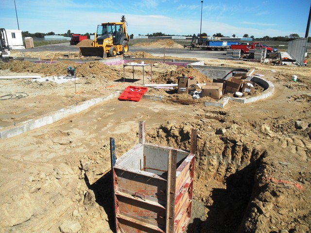 building site with concrete footings in place, backhoe in background
