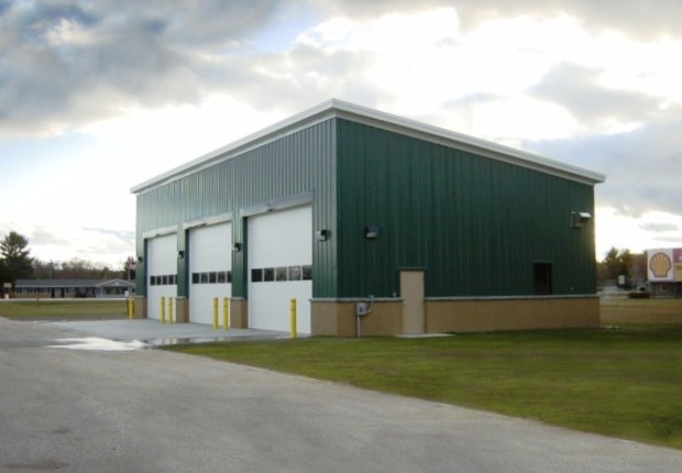 picture of Snow Removal Equipment Building - green metal siding, white vehicle bay doors against a mostly cloudy sky