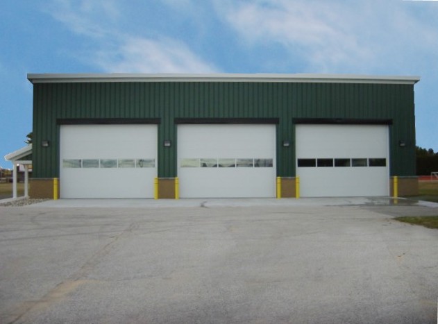 picture of Snow Removal Equipment Building - green metal siding, white vehicle bay doors looking straight at vehicle bays