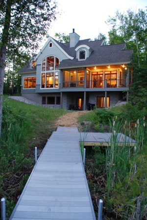picture of custom lakefront cottage in Cheboygan, MI - this exterior photo is of the lakeside elevation of the cottage taken in the early evening - the lights in the home are on, inviting you to come inside and enjoy the view out on Twin Lake