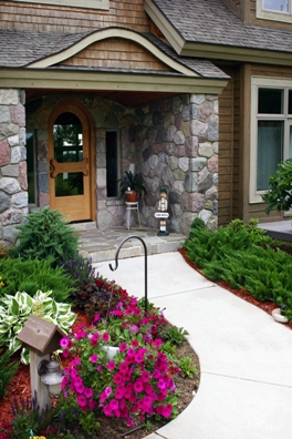 picture of lakeside custom home on Otsego Lake - this exterior photo is of the home's main entrance, with curved walkway leading to stone porch and custom entry door with sidelights set in stone - the curve in the custom door is repeated in the detail over the porch roof