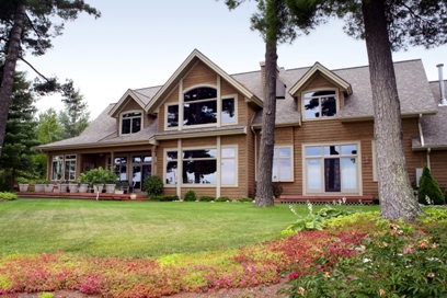 picture of lakeside home on Otsego Lake - this exterior photo was taken of the lakeside elevation - custom windows with unique trim, multiple sets of french doors leading onto outdoor decks overlook a sweeping lawn leading down to the water's edge