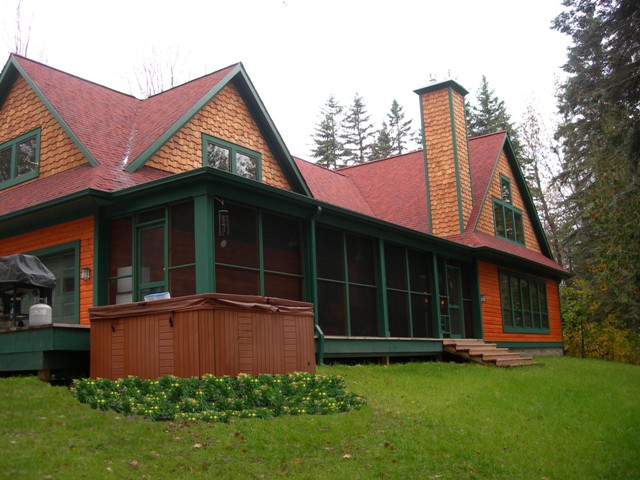 exterior photo of the lakeside elevation of custom waterfront home on Six Mile Lake in East Jordan, MI showing bold natural cedar colors with green trim and red shingle roof