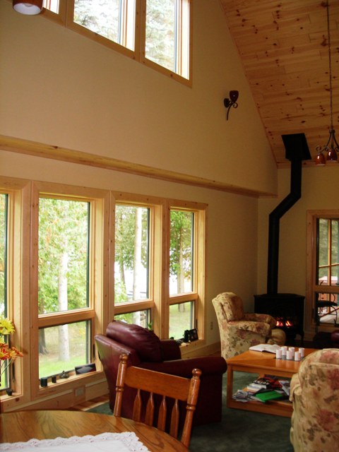 interior photo of the great room, light yellow walls with natural wood ceilings and trim and a view of the lake through the windows