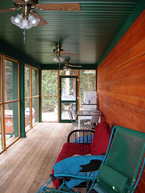the screened porch of this custom home is finished in dark green ceiling and trim with natural cedar walls and an unfinished wood deck