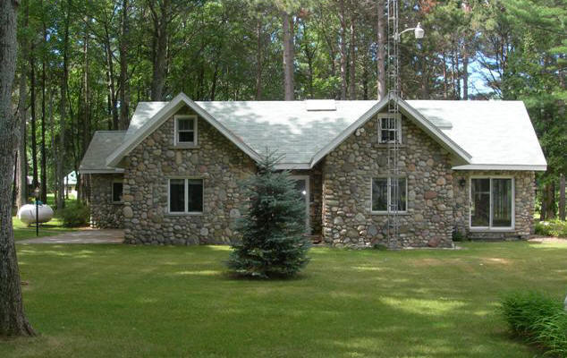 An exterior photo of lakefront home in Lewiston, Michigan, before renovations began.  The home is a total fieldstone exterior with small windows.