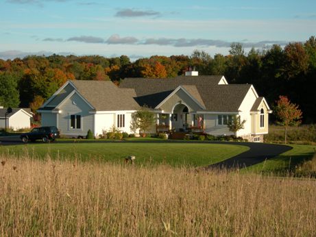 picture of a custom country home in Gaylord, Michigan - this Autumn afternoon exterior photo shows the elevation of the home from the road - curved entry way, muted yellow siding and earth-toned architectural shingles