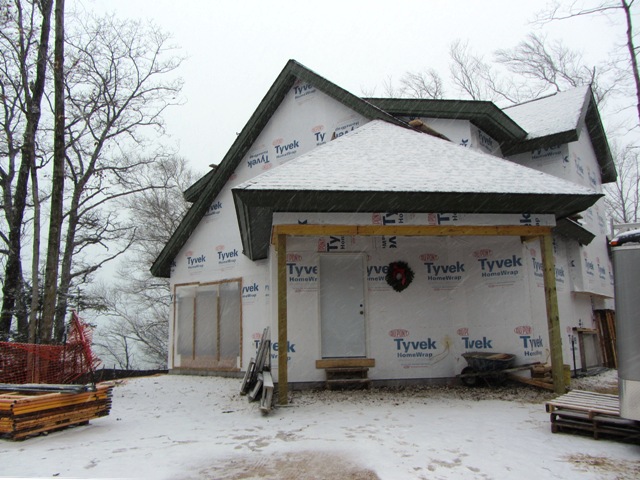 picture of custom home being built on Lake Michigan - snow covered roofs and white tyvek covered house with a Christmas wreath at the front door