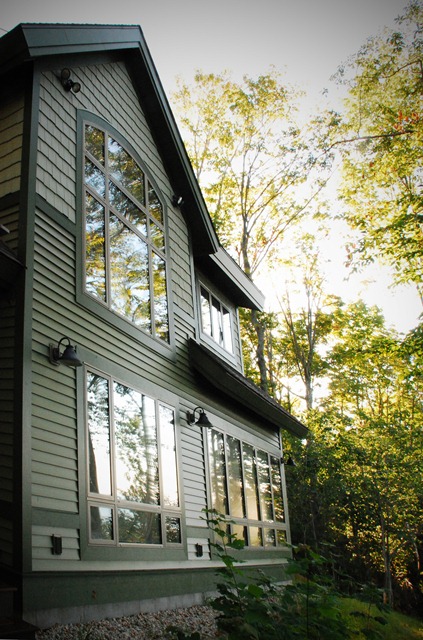 Two-toned green siding, dark green trim and custom windows reflect the late summer trees