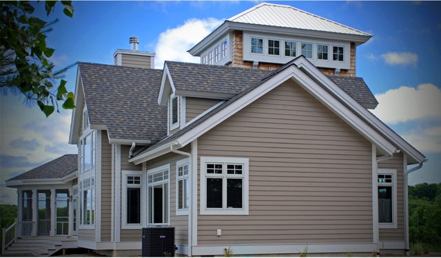 picture of custom home with tan siding, architectural shingle roof, white trim, tower and screened porch