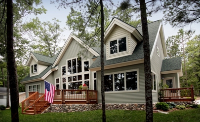 picture of lakeside elevation of custom waterfront home on East Twin Lake in Lewiston MI - grey siding, white trim, dark grey/green shingle roof, wood decks