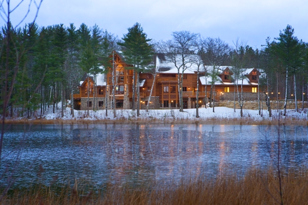 exterior winter photo taken from across the lake at dusk, with lights on in home and reflected in the water surface of Ward Lake