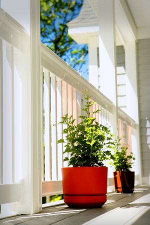 picture of custom home at Mountain Lake Golf Club - this exterior photo was taken from the steps leading up to the upper covered porch, looking down the length of the porch through the white railings - the red planters and foliage really pop against the light grey siding and white trim