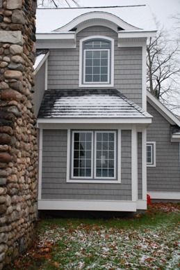 picture of lakeside home in Topinabee, Michigan - this exterior photo shows the home's fieldstone fireplace in the foreground, and custom curved windows on the second floor with matching curved roof detail