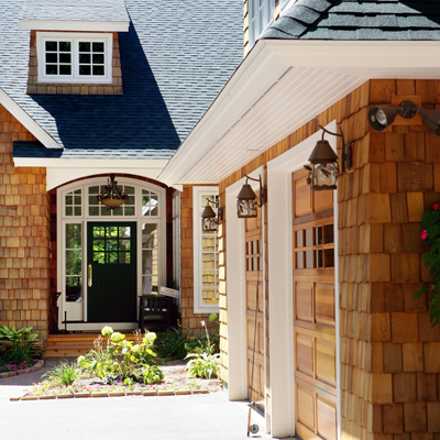 picture of custom home on O'Rourke Lake - this exterior photo was taken looking at the home's main entrance along the front of the garage - note the custom wood garage doors which match the cedar shake siding, the bronze lantern light fixtures on the home's exterior, and yes that's a fly fishing rod propped up against the garage