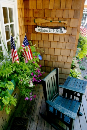 picture of lakeside custom home on O'Rourke Lake - this is an exterior photo of an outdoor sitting area with weathered wood plank floor and window flower boxes, natural cedar siding on home with white window trim