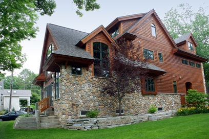 picture of lakeside custom home on Otsego Lake - this exterior photo was taken of the side-yard elevation showing fieldstone and wood siding with architectural shingles, custom windows, raised planters and stone steps leading up to the entrance on the lakeside elevation
