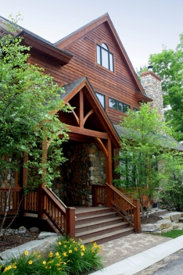 picture of custom lakeside home on Otsego Lake - this exterior photo is of the road side entry, which is the main entrance to the home - fieldstone and wood siding are complimented by delicate landscaping, soft trees flank the steps leading up to the covered porch