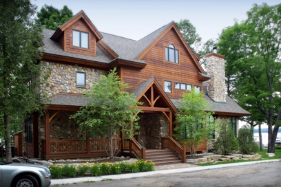 picture of custom lakeside home on Otsego Lake - this exterior photo was taken from the road side elevation with lake in the background - the home's exterior is fieldstone and wood siding with wrap-around covered porch