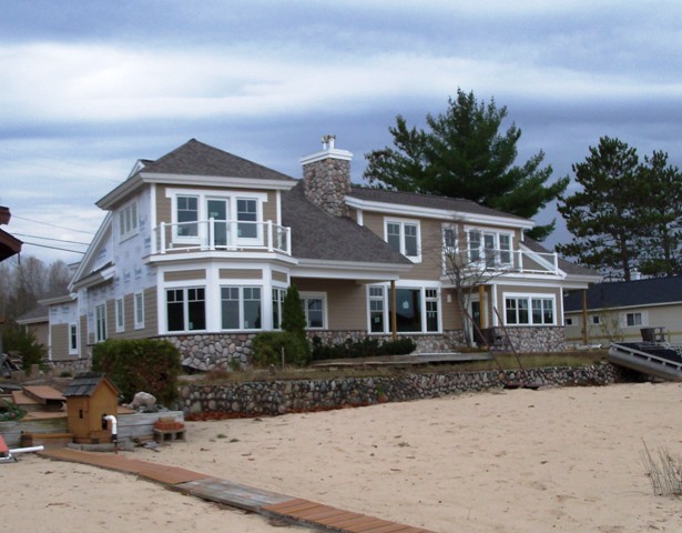 picture of lakeside elevation of custom home under construction on the South end of Otsego Lake - the tan siding and white trim provide contrast against the fieldstone on the lower walls.