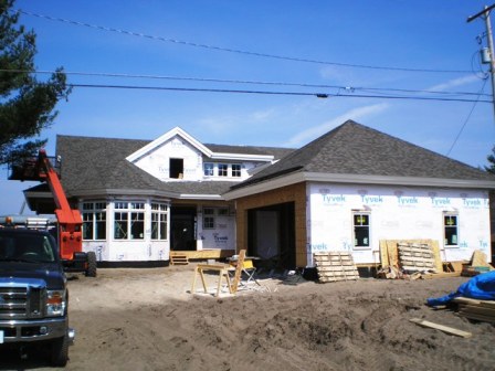 picture of custom home under construction on the South end of Otsego Lake - windows and doors are being installed, house wrap is almost finished and roof shingles are on