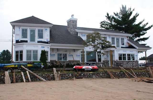 picture of lakeside elevation of custom home under construction on the South end of Otsego Lake - fieldstone is installed on lower walls and chimney, and the home is almost ready for siding installation to begin