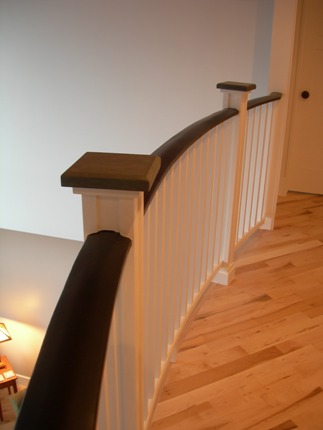 picture of waterfront home on Twin Lakes in Cheboygan, Michigan - this interior photo was taken on the second floor of the cottage, looking along the curved balcony railing above the living area below - the dark wood of the top rail contrasts nicely with the light stained hardwood floors and iced-pastel wall colors