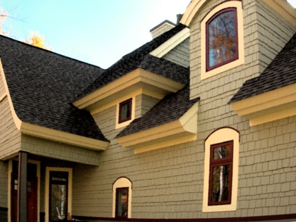 picture of waterfront home on Twin Lakes in Cheboygan, Michigan - this exterior photo shows the cottage's many architectural details, from the light gray shake siding and mixed red and gray architectural shingle roof to the white soffits framing red trim on the windows - there are angles and curves on every elevation of this custom cottage