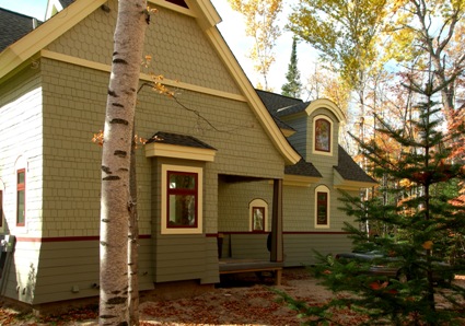 picture of waterfront home on Twin Lakes in Cheboygan, Michigan - this exterior photo shows two-tone gray siding separated by a trim band in red which is repeated in the trim on the windows - the white soffits and separation trim in the upper portion of the siding draw your eye up to see curves and angles throughout the cottage's construction