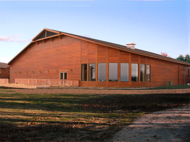 picture of Bay Mills Conference Center at dining room and outdoor deck - the building has wood plank siding and a decorative cmu retainer wall