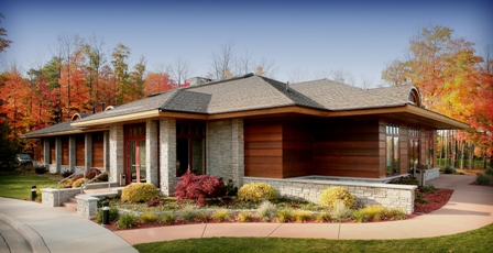 exterior picture of UAW Black Lake Golf Course Clubhouse main entry and side patio - dark wood siding, stone accents and wood trim, grey roof with backdrop of autumn leafed trees